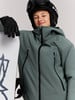 Junge im Skianzug und Helm hält Snowboard.