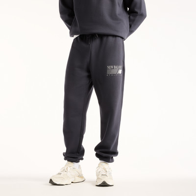 Ein Mann trägt eine dunkelblaue Jogginghose mit New Balance Logo und weiße Sneaker. Ein Mann trägt eine dunkelblaue Jogginghose mit New Balance Logo und weiße Sneaker.