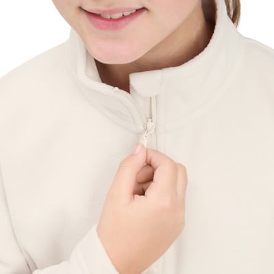 Ein Mädchen schließt den Reißverschluss einer cremefarbenen Fleecejacke.