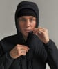 Eine Frau schließt eine schwarze Kapuzenjacke und trägt eine schwarze Mütze.