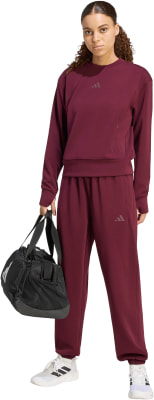 Eine Frau in burgunderfarbener Sportkleidung hält eine schwarze Tasche und trägt weiße Turnschuhe.