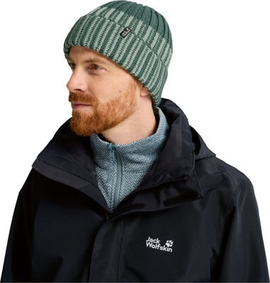 Ein Mann mit rotem Bart trägt eine grüne gestreifte Mütze und eine dunkle Jacke. Ein Mann mit rotem Bart trägt eine grüne gestreifte Mütze und eine dunkle Jacke.