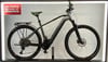 Graues Cube E-Bike mit Gepäckträger und Schutzblechen auf dunklem Ständer.