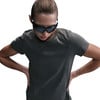 Eine Frau in einem dunklen T-Shirt und einer Sonnenbrille, die die Hände in die Hüften stützt.
