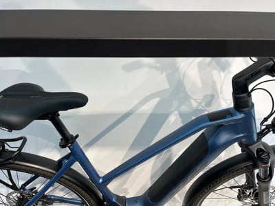 Ein blaues E-Bike mit schwarzem Sattel und Schutzblechen steht an einer Wand.