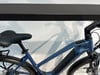 Ein blaues E-Bike mit schwarzem Sattel und Schutzblechen steht an einer Wand.