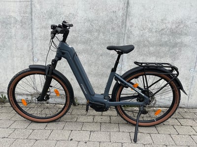 Ein graues E-Bike mit braunen Reifen und schwarzem Gepäckträger steht an einer Wand. Ein graues E-Bike mit braunen Reifen und schwarzem Gepäckträger steht an einer Wand.