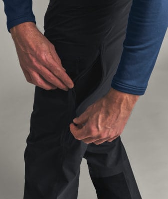 Ein Mann schließt den Reißverschluss einer schwarzen Hose mit einer dunkelblauen Jacke.