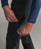 Ein Mann schließt den Reißverschluss einer schwarzen Hose mit einer dunkelblauen Jacke.