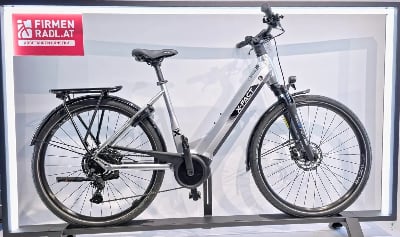Silbernes X-FACT E-Bike mit Gepäckträger und Schutzblechen auf einem Ständer. Silbernes X-FACT E-Bike mit Gepäckträger und Schutzblechen auf einem Ständer.