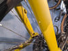 Details eines gelben Fahrradrahmens mit Kette und Speichen.