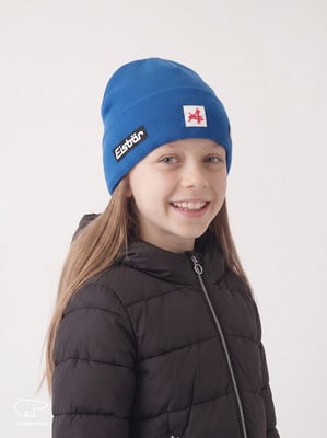 Ein Mädchen in einer blauen Mütze und einem schwarzen Daunenmantel lächelt. Ein Mädchen in einer blauen Mütze und einem schwarzen Daunenmantel lächelt.