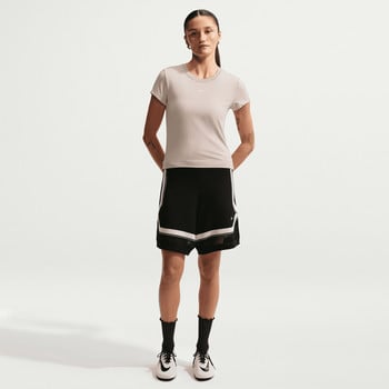 Eine Frau in einem beigen T-Shirt und schwarzen Netzshorts steht vor einem weißen Hintergrund.
