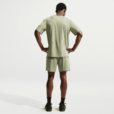 Rückansicht eines Mannes in grünem T-Shirt und Shorts mit Händen in den Hüften.