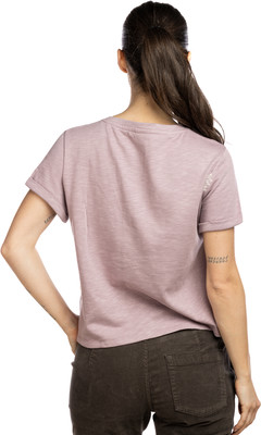 Eine Frau in einem rosa T-Shirt und braunen Hosen mit Tätowierungen am Arm.