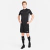 Ein Mann im schwarzen Fußballtrikot und Shorts steht mit den Händen in den Hüften.