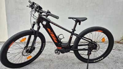 Ein schwarzes KTM E-Bike mit orangefarbenen Details steht vor einer Wand. Ein schwarzes KTM E-Bike mit orangefarbenen Details steht vor einer Wand.