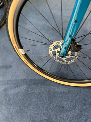 Detail eines Fahrradrades mit Scheibenbremse und beiger Bereifung.