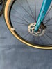 Detail eines Fahrradrades mit Scheibenbremse und beiger Bereifung.