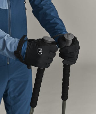 Eine Person in blauer Kleidung hält Trekkingstöcke in schwarzen Handschuhen.