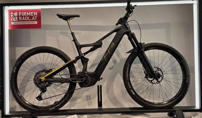 Ein schwarzes E-Mountainbike mit Federung und goldenen Details steht auf einem Ständer. Ein schwarzes E-Mountainbike mit Federung und goldenen Details steht auf einem Ständer.