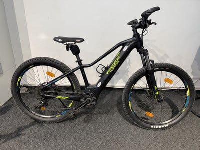 Ein schwarzes E-Bike mit Federung und breiten Reifen steht auf einem dunklen Teppich. Ein schwarzes E-Bike mit Federung und breiten Reifen steht auf einem dunklen Teppich.