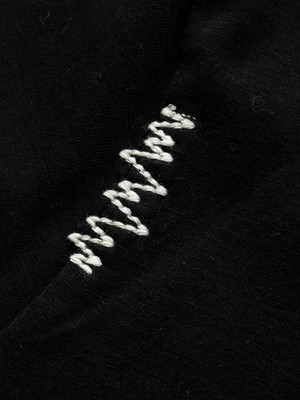 Schwarzer Stoff mit weißem Zickzackstich auf der Oberfläche. Schwarzer Stoff mit weißem Zickzackstich auf der Oberfläche.