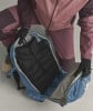 Eine Person in Handschuhen verstaut eine schwarze Jacke in einem blauen Rucksack.
