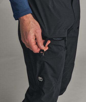 Eine Männerhand hält eine Schlaufe am Reißverschluss einer schwarzen Hose.