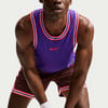 Mann in lila Nike Trikot und dunkler Hose mit Streifen.