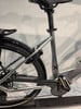 Rückseite eines silbernen E-Bikes mit Kette, Pedal und Schutzblech.
