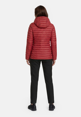 Rückansicht einer Frau in einer roten Steppjacke mit Kapuze und schwarzen Hosen. Rückansicht einer Frau in einer roten Steppjacke mit Kapuze und schwarzen Hosen.