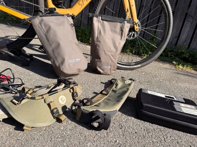 Zwei Fahrradtaschen hängen am Hinterrad, weiteres Zubehör liegt am Boden. Zwei Fahrradtaschen hängen am Hinterrad, weiteres Zubehör liegt am Boden.