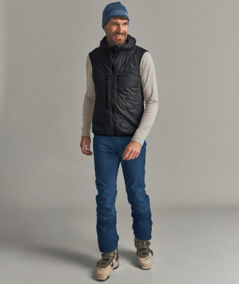 Ein Mann in einer Daunenweste, Mütze und Skihose posiert lächelnd. Ein Mann in einer Daunenweste, Mütze und Skihose posiert lächelnd.
