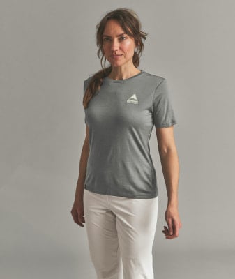 Eine Frau in einem grauen T-Shirt und weißer Hose steht vor einem grauen Hintergrund. Eine Frau in einem grauen T-Shirt und weißer Hose steht vor einem grauen Hintergrund.