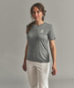 Eine Frau in einem grauen T-Shirt und weißer Hose steht vor einem grauen Hintergrund.
