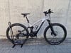 Ein silbernes E-Bike mit schwarzen Details steht auf einem Ständer vor einer Wand.