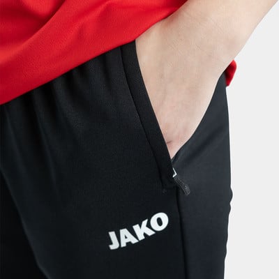 Detail einer schwarzen Hose mit JAKO-Logo und einer Hand in der Tasche. Detail einer schwarzen Hose mit JAKO-Logo und einer Hand in der Tasche.