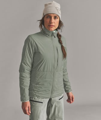 Eine Frau in einer grün-grauen Jacke und Mütze steht vor grauem Hintergrund. Eine Frau in einer grün-grauen Jacke und Mütze steht vor grauem Hintergrund.