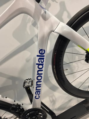 Detail eines weißen Fahrradrahmens mit Cannondale-Logo und schwarzem Rad. Detail eines weißen Fahrradrahmens mit Cannondale-Logo und schwarzem Rad.