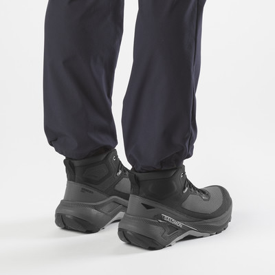Rückansicht von Füßen in schwarzen Salomon-Wanderschuhen und dunklen Hosen.