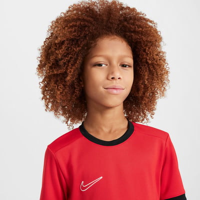Ein Junge mit lockigem Haar trägt ein rotes T-Shirt mit Nike-Logo.