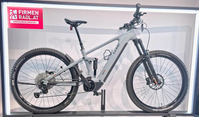 Graues Cube E-Bike mit Federung und Schutzblechen auf einem Ausstellungsständer. Graues Cube E-Bike mit Federung und Schutzblechen auf einem Ausstellungsständer.