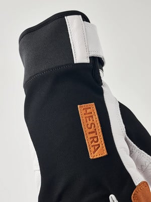 Schwarze Hestra-Skihandschuhe mit weißen Lederdetails und Logo. Schwarze Hestra-Skihandschuhe mit weißen Lederdetails und Logo.