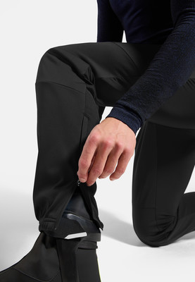 Ein Mann schließt den Reißverschluss an einer schwarzen Skihose am Stiefel. Ein Mann schließt den Reißverschluss an einer schwarzen Skihose am Stiefel.