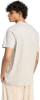 Ein Mann in einem beigen T-Shirt und Jogginghose mit lockigem Haar.