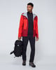Ein Mann in roter Jacke und schwarzer Hose hält einen Rucksack.