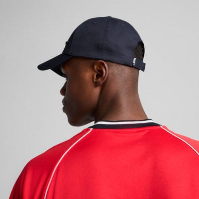 Ein Mann trägt eine dunkelblaue Kappe und ein rotes Shirt mit weißen Akzenten.