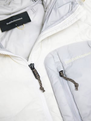 Detail einer Jacke mit Peak Performance Logo, Reißverschlüssen und Kordel.