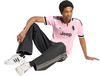 Ein junger Mann in einem rosa T-Shirt und Jeans sitzt auf dem Boden.